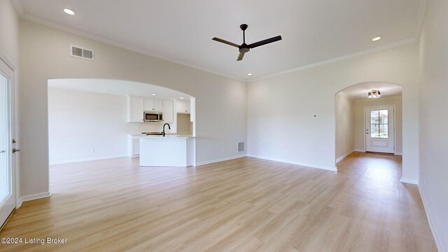 unfurnished living room with ceiling fan with notable chandelier, light hardwood / wood-style flooring, and ornamental molding