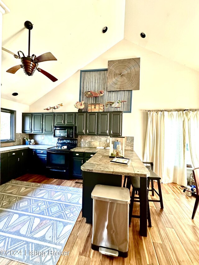 kitchen featuring backsplash, light hardwood / wood-style floors, vaulted ceiling, and black appliances