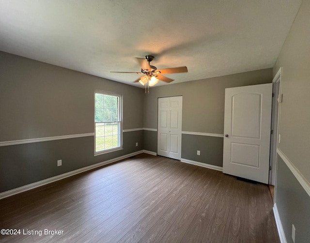 unfurnished bedroom featuring a ceiling fan, a closet, baseboards, and dark wood finished floors