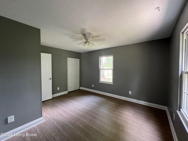 unfurnished bedroom with baseboards, dark wood-style floors, a closet, and ceiling fan