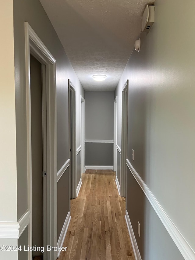 hall featuring baseboards, light wood-type flooring, and a textured ceiling