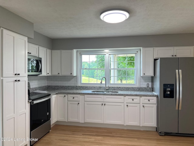 kitchen with a sink, white cabinetry, light wood-style flooring, and appliances with stainless steel finishes