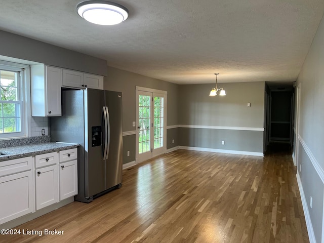 kitchen with stainless steel fridge, light wood-type flooring, white cabinets, decorative backsplash, and an inviting chandelier