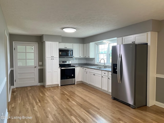 kitchen featuring white cabinetry, a sink, appliances with stainless steel finishes, and light wood-style floors