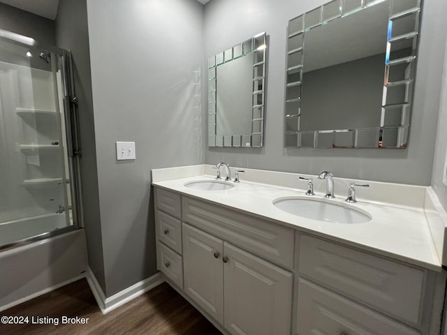 full bath featuring double vanity, enclosed tub / shower combo, wood finished floors, and a sink