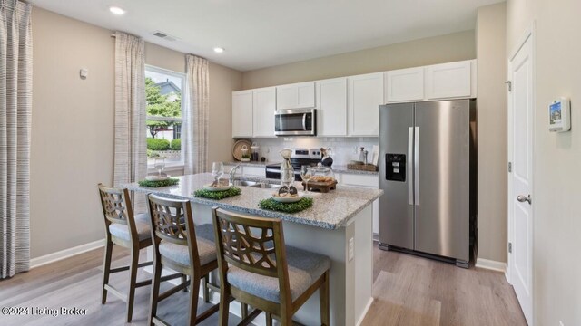 kitchen with an island with sink, appliances with stainless steel finishes, a breakfast bar area, and white cabinets