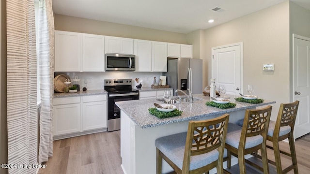 kitchen with appliances with stainless steel finishes, a kitchen island with sink, light hardwood / wood-style flooring, and white cabinets