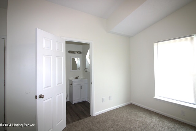 unfurnished bedroom featuring dark carpet, connected bathroom, and vaulted ceiling