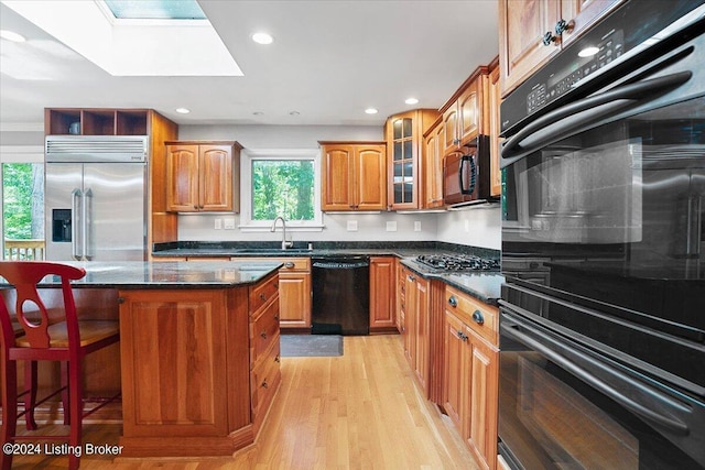 kitchen featuring a center island, black appliances, sink, a skylight, and a healthy amount of sunlight