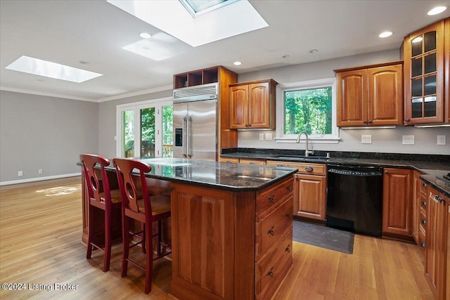 kitchen featuring a skylight, stainless steel built in refrigerator, sink, black dishwasher, and a kitchen island