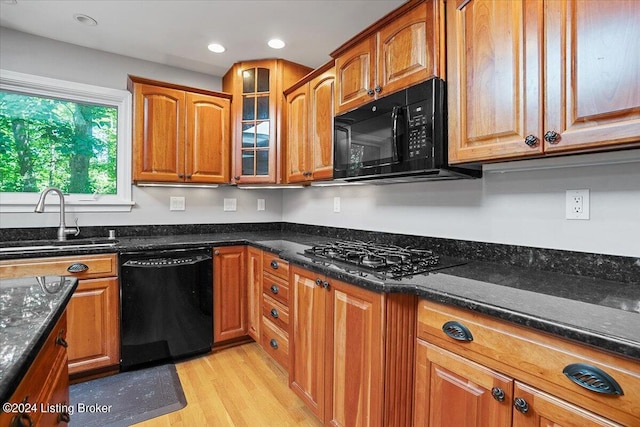 kitchen with black appliances, dark stone countertops, light wood-type flooring, and sink