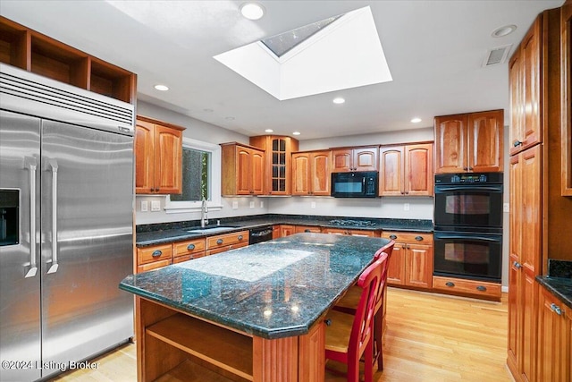 kitchen featuring black appliances, sink, a skylight, light wood-type flooring, and a kitchen island