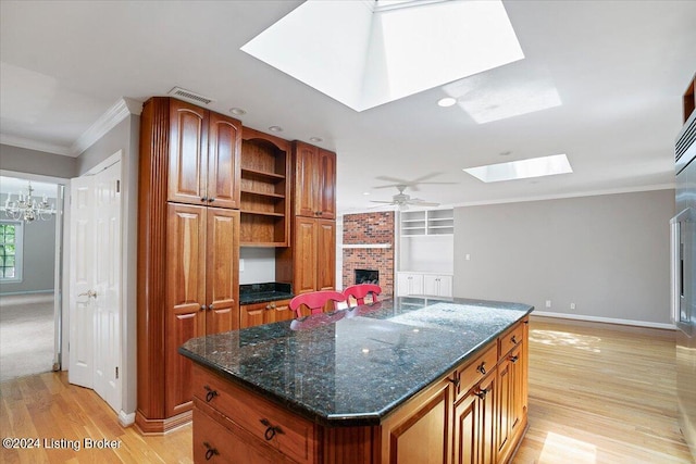 kitchen with a center island, crown molding, a skylight, light wood-type flooring, and a fireplace