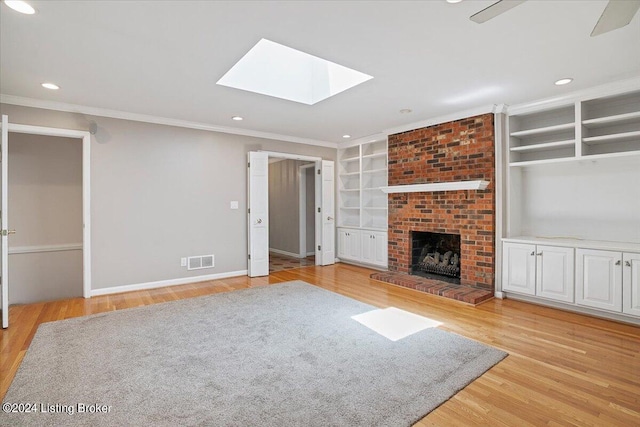 unfurnished living room featuring a fireplace, built in shelves, a skylight, and light hardwood / wood-style flooring