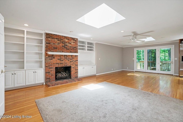 unfurnished living room with a skylight, a brick fireplace, ornamental molding, ceiling fan, and light hardwood / wood-style flooring