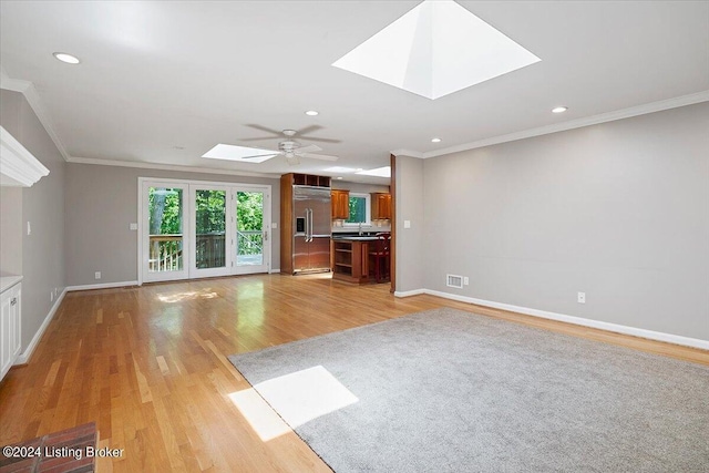 unfurnished living room with light wood-type flooring, a skylight, crown molding, and sink