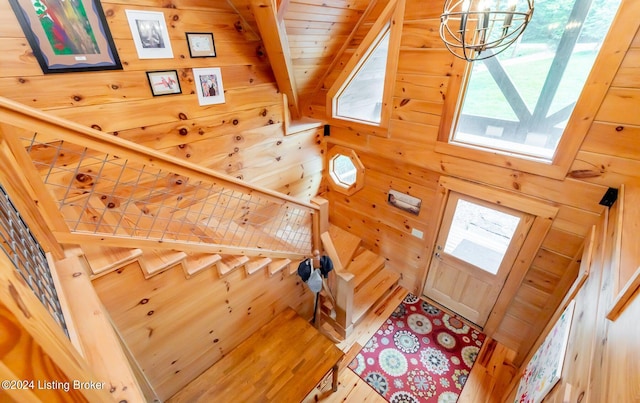 stairs with hardwood / wood-style flooring, beam ceiling, wooden ceiling, a chandelier, and wood walls