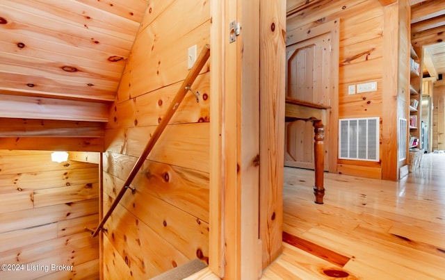 staircase with wood walls, lofted ceiling, hardwood / wood-style floors, and wooden ceiling