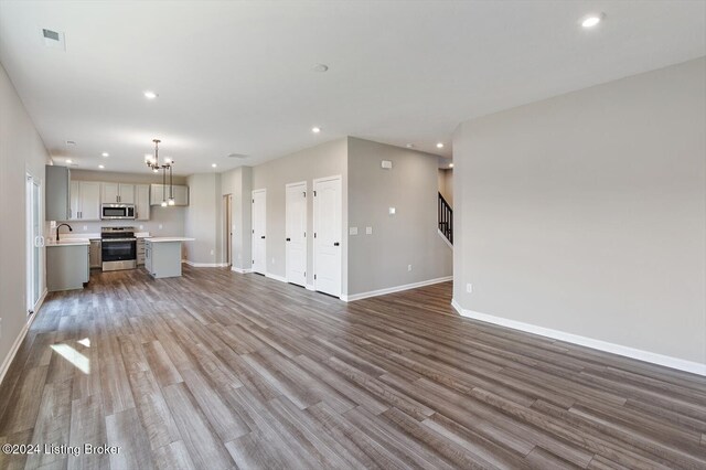 unfurnished living room featuring sink, wood-type flooring, and a notable chandelier