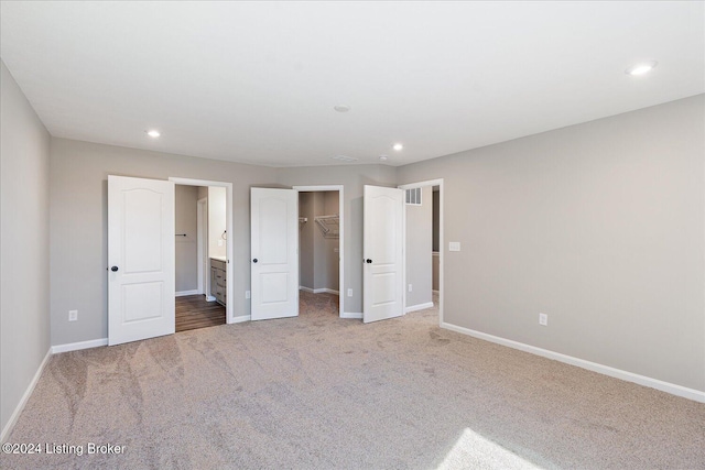 unfurnished bedroom featuring a spacious closet, ensuite bath, a closet, and carpet floors