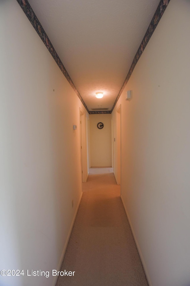 hallway with light carpet and a textured ceiling