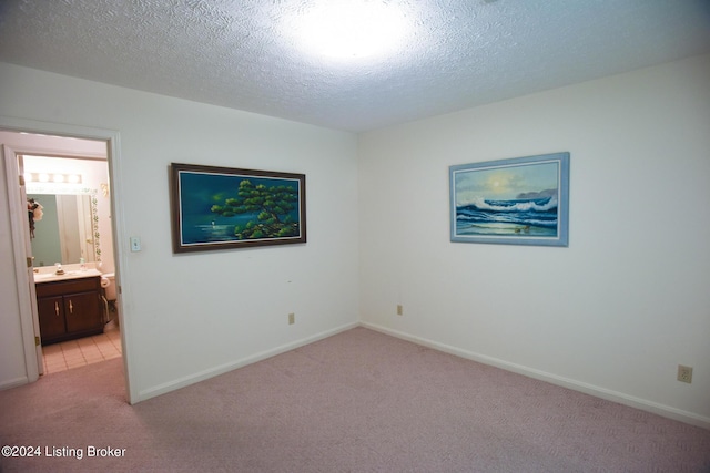 unfurnished bedroom featuring sink, ensuite bathroom, light colored carpet, and a textured ceiling