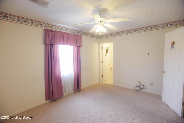 empty room with ceiling fan, light colored carpet, and a textured ceiling