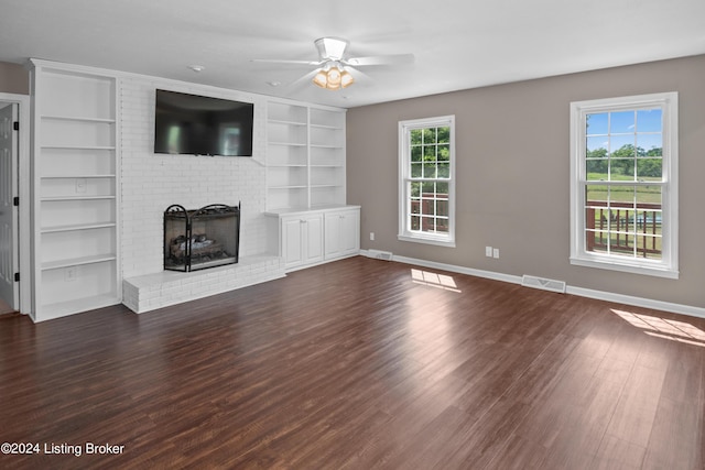 unfurnished living room featuring a brick fireplace, dark wood-type flooring, built in features, and ceiling fan