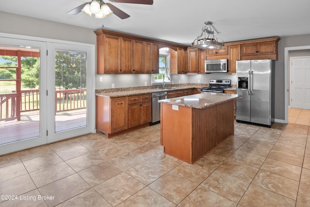 kitchen with sink, hanging light fixtures, stainless steel appliances, light stone countertops, and a kitchen island