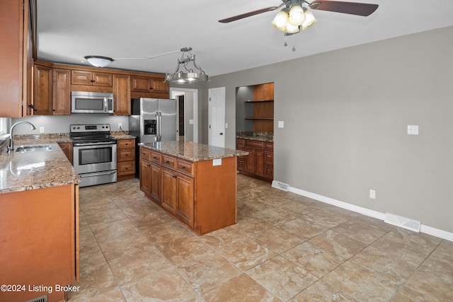 kitchen with sink, light stone counters, decorative light fixtures, appliances with stainless steel finishes, and a kitchen island