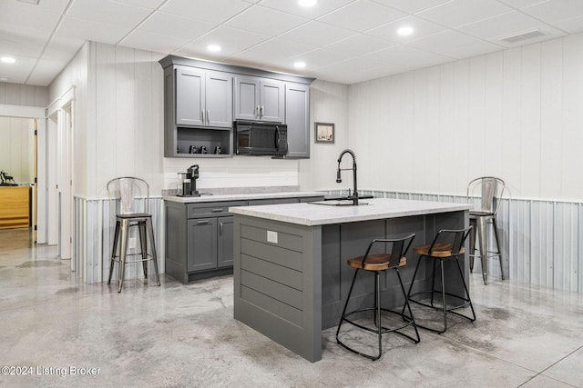 kitchen with wood walls, sink, gray cabinetry, a kitchen bar, and a center island with sink