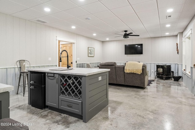 interior space with gray cabinets, a wood stove, sink, and wooden walls