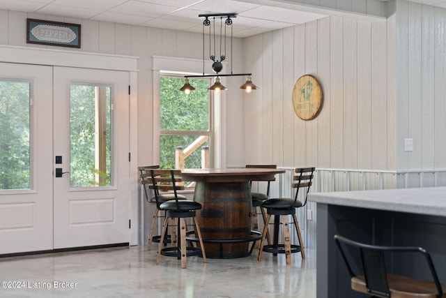 dining space with a paneled ceiling, wooden walls, and french doors