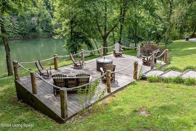 wooden terrace with a water view, a lawn, and an outdoor fire pit