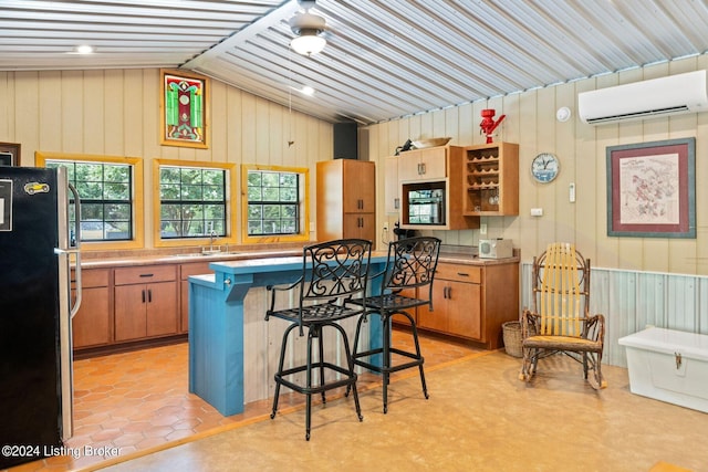 kitchen with a breakfast bar, sink, a wall mounted air conditioner, wooden walls, and stainless steel fridge