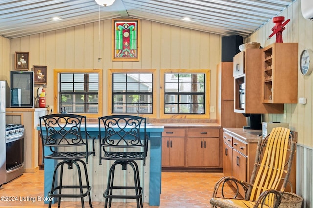 kitchen featuring gas stove, a healthy amount of sunlight, light tile patterned floors, and wooden walls