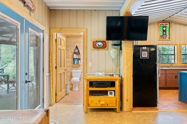 interior space featuring stainless steel refrigerator, a wealth of natural light, sink, and wood walls