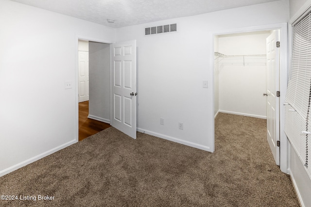 unfurnished bedroom with dark colored carpet, a spacious closet, a textured ceiling, and a closet