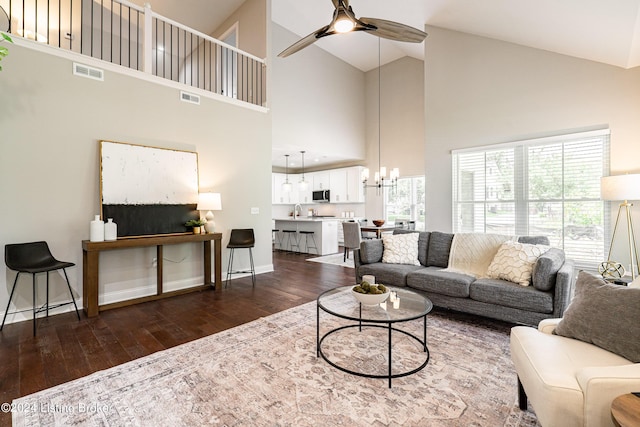 living room with dark wood-style flooring, visible vents, baseboards, and ceiling fan with notable chandelier