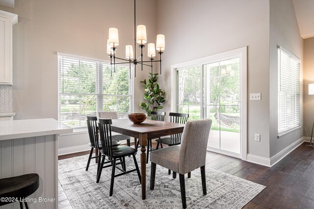 dining space featuring dark wood-type flooring, a notable chandelier, a towering ceiling, and baseboards