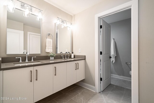 bathroom with marble finish floor, a sink, toilet, and double vanity