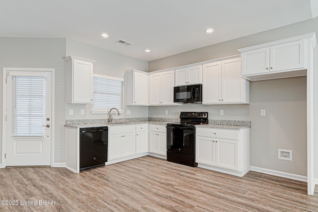 kitchen with sink, light stone countertops, black appliances, white cabinets, and light wood-type flooring