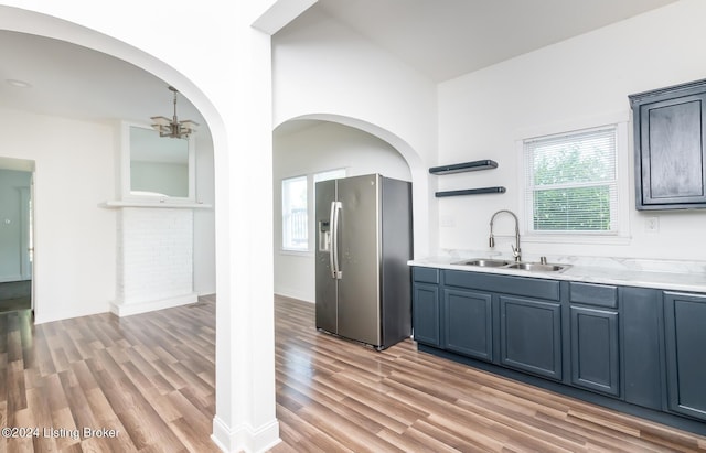 kitchen with sink, blue cabinets, light wood-type flooring, stainless steel fridge with ice dispenser, and a chandelier