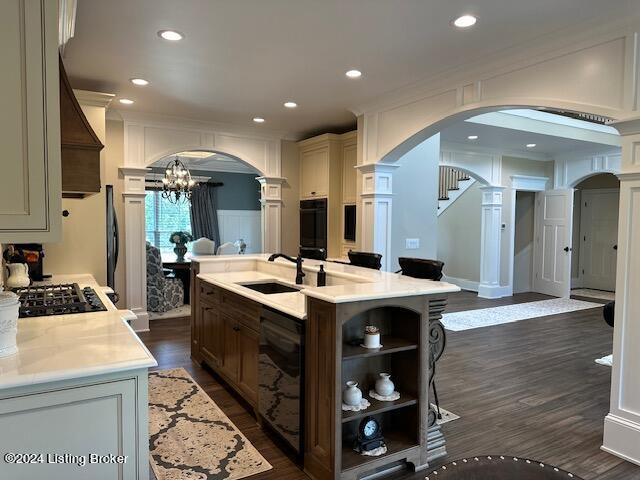 kitchen with a kitchen island with sink, dark wood-type flooring, light stone countertops, a chandelier, and sink