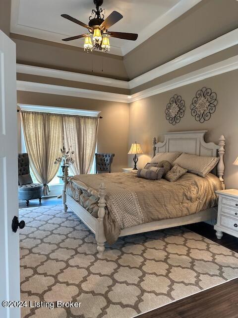 bedroom with ceiling fan, hardwood / wood-style floors, a raised ceiling, and crown molding