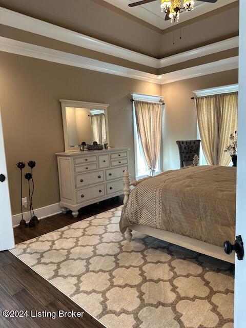 bedroom with ceiling fan, dark wood-type flooring, a tray ceiling, and ornamental molding