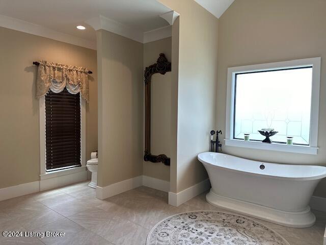 bathroom featuring toilet, vaulted ceiling, tile patterned floors, a tub, and ornamental molding