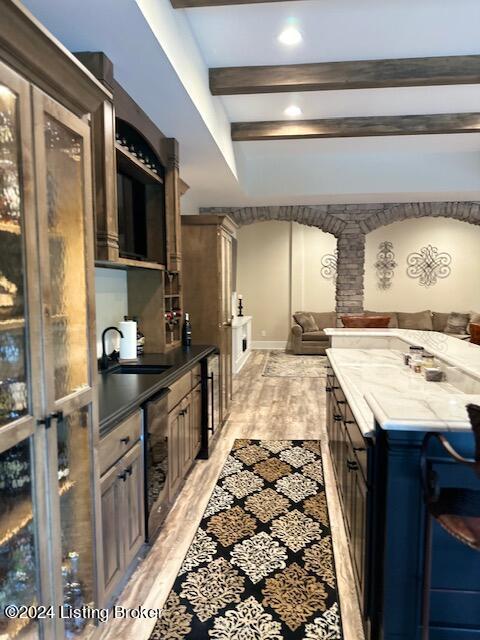 kitchen with a breakfast bar area, sink, dark stone counters, dark brown cabinetry, and beamed ceiling