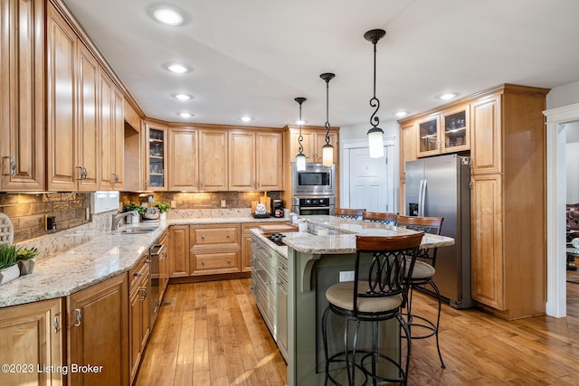 kitchen featuring a kitchen island, appliances with stainless steel finishes, hanging light fixtures, light stone countertops, and light wood-type flooring