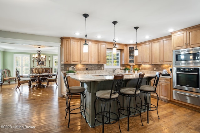 kitchen with pendant lighting, wood-type flooring, a center island, light stone counters, and stainless steel appliances